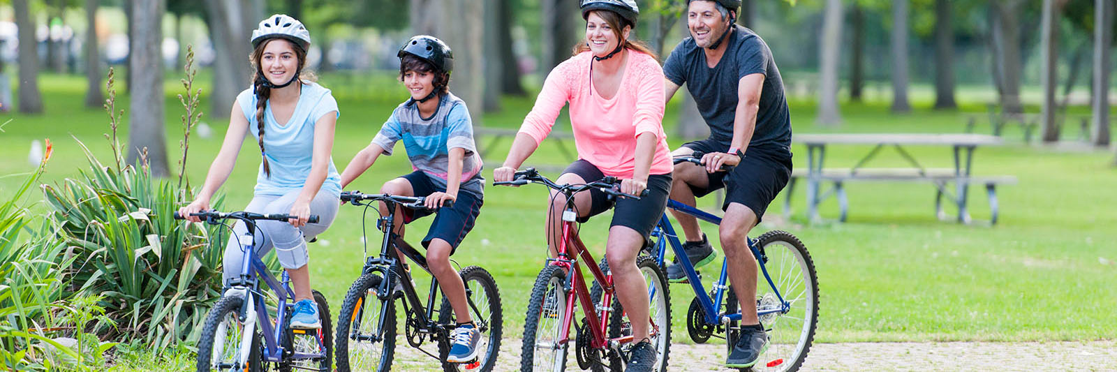 family-riding-bikes-through-park-1600x533