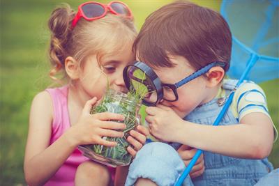 kids using magnifying glass to study jar of grass