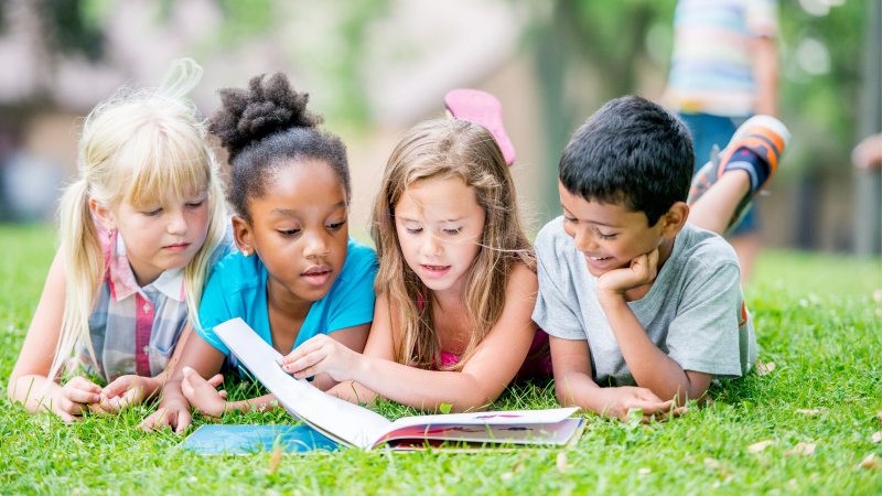 Four children reading a book together outside