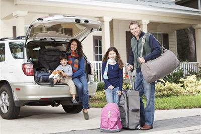 family with suitcases at car trunk in front of house