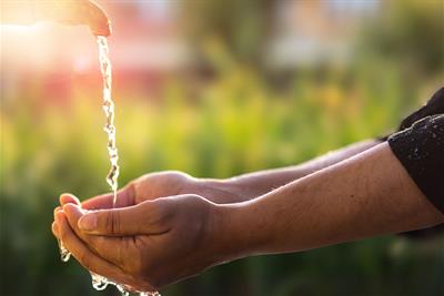 hands cupping water from outdoor faucet backlit sunlight