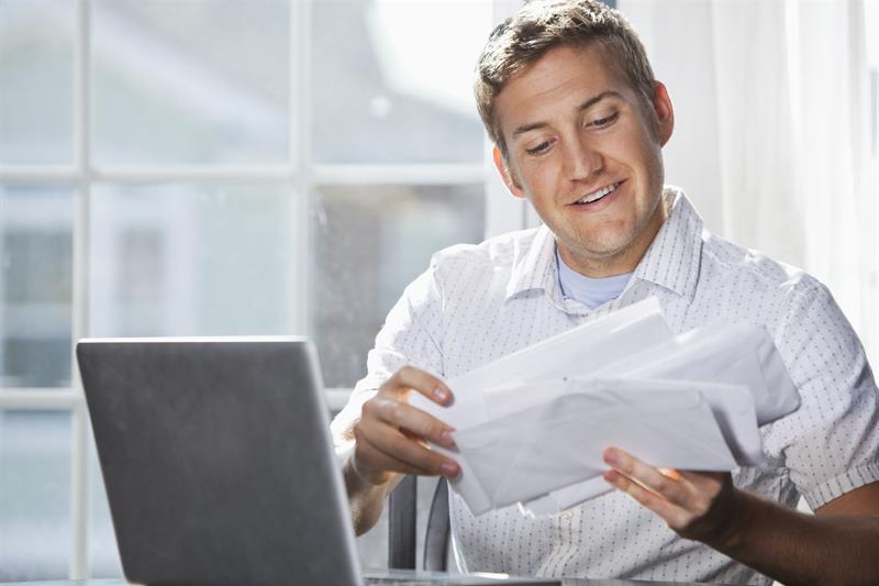 man reading mail and paying bills with laptop
